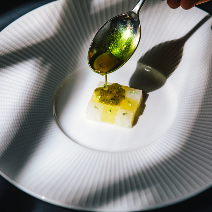 A dish at 2 Michelin Star Restaurant Vinkeles, in luxury boutique hotel The Dylan Amsterdam, member of the Leading Hotels of the World. Executive Jurgen van der Zalm pouring en sauce on the dish. Dish on a white big plate.