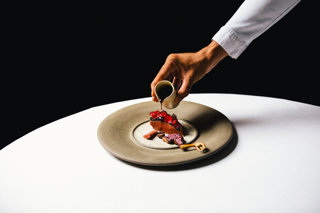 ANJOU PIGEON - Ponzu, red onion, sour cherry, rose, Cusco Chunco 100%. A dish at 2 Michelin star Restaurant Vinkeles, in luxury boutique hotel The Dylan Amsterdam.  Executive Chef Jurgen van der Zalm pouring the sauce on the dish. 