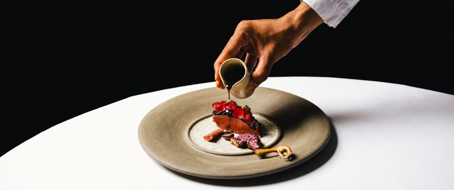 ANJOU PIGEON - Ponzu, red onion, sour cherry, rose, Cusco Chunco 100%. A dish at 2 Michelin star Restaurant Vinkeles, in luxury boutique hotel The Dylan Amsterdam.  Executive Chef Jurgen van der Zalm pouring the sauce on the dish. 